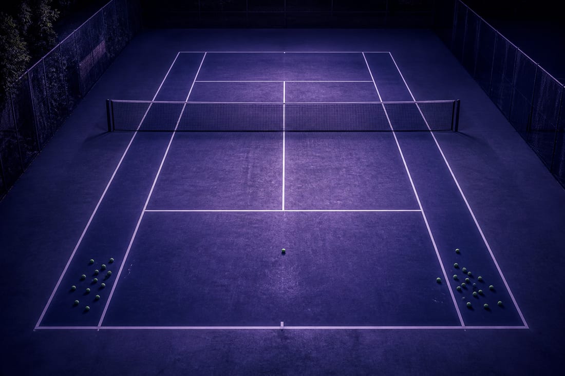 A tennis court from overhead with two clusters of balls near each baseline sideline and a single ball on the centre mark between them