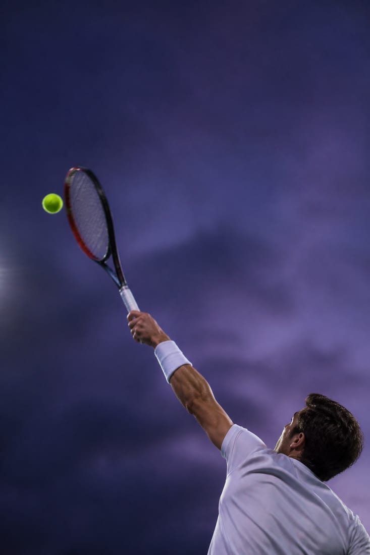 A server mid-motion with the ball tossed to the left of the head and slightly behind, the racquet swinging up across it