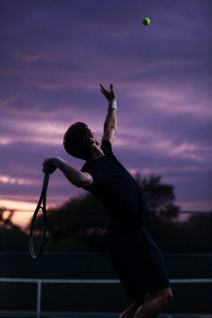 A server at full extension with the racquet dropped deep behind the back, knees loaded and the tossing arm high