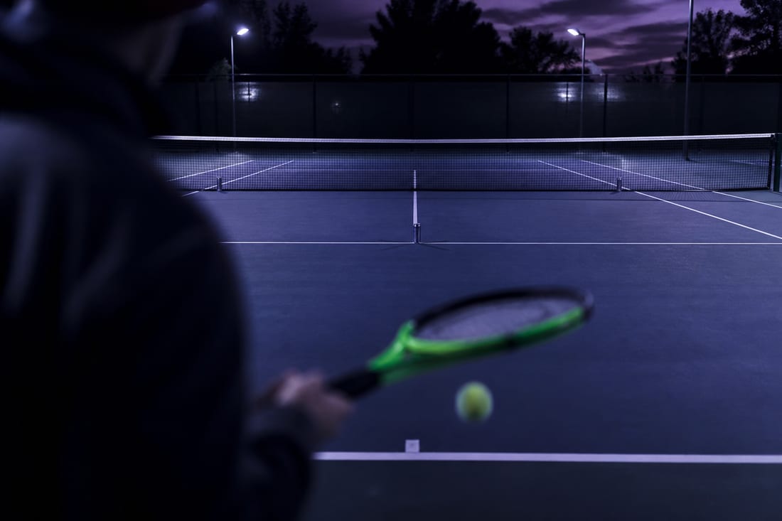 A tennis service box with three metal cans standing as targets, one in each back corner and one on the centre service line, seen from behind the baseline