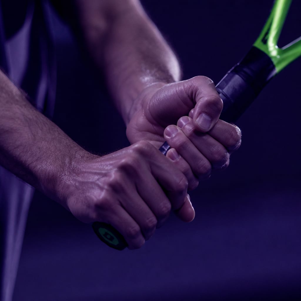 Both hands on a racquet handle in a two-handed backhand grip, the dominant hand below in a continental position and the non-dominant hand above